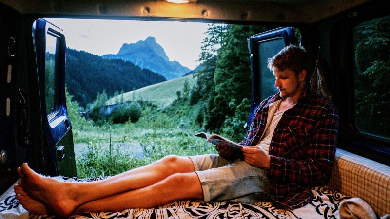 Man reads book in the back of van while camping